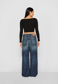 Fekete, hosszú ujjú crop top, széles szárú kék farmernadrággal, amely halványuló hatást és látható hátsó zsebeket tartalmaz.