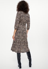 Schwarz-beige gemustertes Kleid mit Dreiviertelärmeln, Frill-Saum und tailliertem Schnitt, kombiniert mit schwarzen knielangen Stiefeln.
