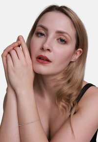 Primo piano di una persona con capelli biondi, che indossa una maglia nera, mostrando un delicato bracciale d'argento al polso, con piccoli accenti trasparenti.