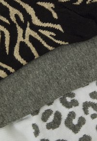 Three folded pairs of socks: one in black with beige animal print, one in gray textured knit, and one in white with black leopard spots.