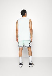 Top bez rukávů v bílé barvě, mátově zelené síťované kraťasy s černým lemem, bílé ponožky a černé tenisky. Jednoduchý atletický design, lehký materiál.