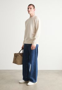 Beige ullgenser, avslappet passform; løse blå denimjeans; hvite joggesko; brun veske med doble håndtak; minimalistisk design.