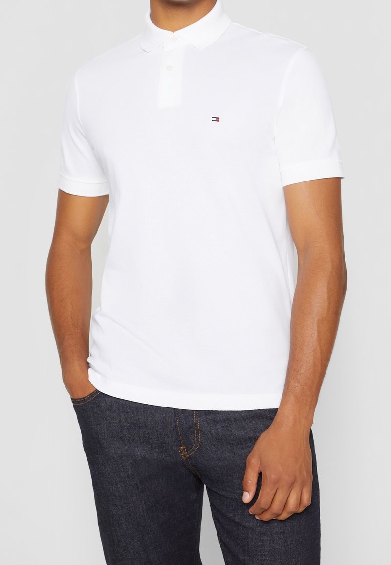 Polo-shirt blanc avec un col classique et des manches courtes. Présente un petit logo sur la poitrine. Fabriqué en tissu doux et respirant.