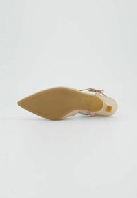 Sandale nude à talons avec un bout pointu, boucle décorative et une semelle en plastique lisse. Logo estampé sur la semelle intérieure.