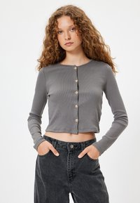 Grå langærmet cropped cardigan lavet af ribbet stof, med en rund halsudskæring og fem guld dekorationsknapper foran.