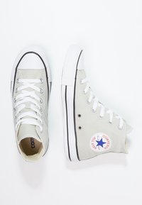 Baskets montantes en toile gris clair, avec des lacets blancs, une semelle en caoutchouc noire et un logo circulaire classique en accent.