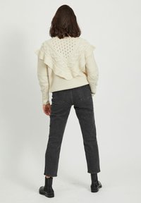 Pull tricoté couleur crème avec un ourlet à volants et des motifs texturés, assorti à un jean gris foncé et des bottines.