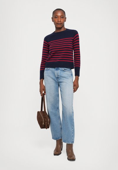 Navy and red striped sweater with a round neckline, paired with light blue jeans and brown ankle boots. Model holds a brown handbag.