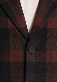 Hnědý a černý kostkovaný vlněný blazer s klopou, vybavený černým knoflíkem a měkkou strukturou.