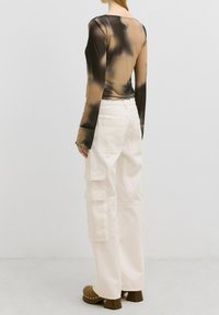 Transparante blouse met lange mouwen in een bruin en beige tie-dye patroon, gecombineerd met witte cargobroek met meerdere zakken en wijde pijpen.