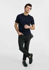 Granatowa koszulka z krótkim rękawem w połączeniu z czarnymi dżinsami i czarnymi sneakersami. Koszulka ma prosty, klasyczny design.