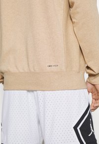 Sweat-shirt beige avec le texte "DRI-FIT" associé à un short de sport blanc perforé avec un patch logo Jordan noir sur le côté.
