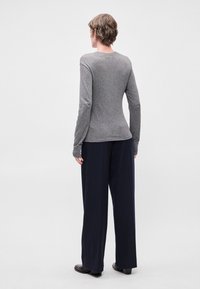 Camisa de manga longa cinza com decote redondo, combinada com calças largas com riscas azul-marinho. Tecido suave e ajuste confortável.