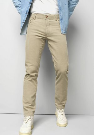 Khaki chinos made of cotton with a slim fit design. Features five pockets, a button closure, and a smooth texture. Paired with white sneakers.