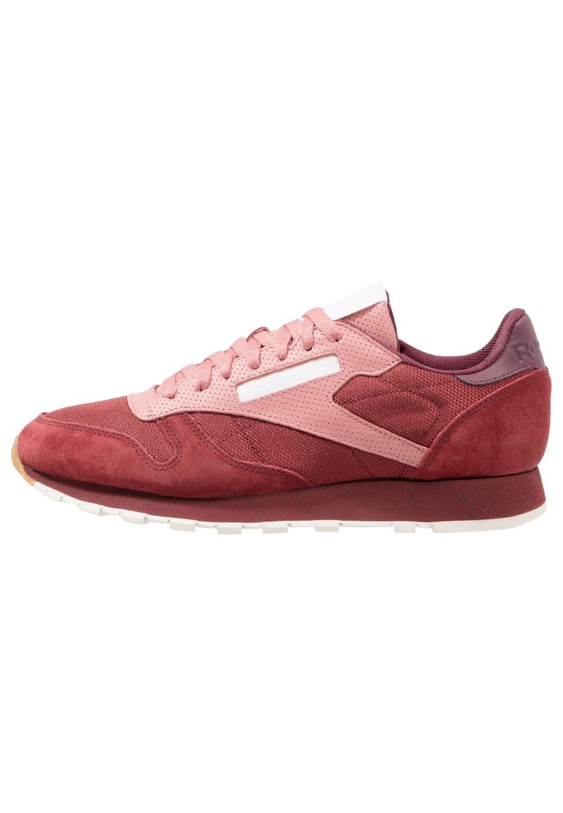 Chaussure de sport rose et rouge en une combinaison de matériaux en suède et en mesh, avec un accent blanc et une semelle en caoutchouc texturée.