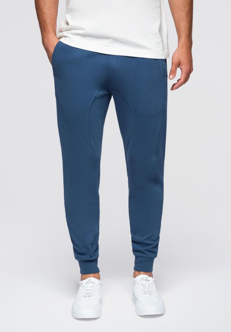 Donkerblauwe joggingsbroek met een taps toelopende pasvorm, gemaakt van zachte stof, met zijzakken en geribbelde boorden, gecombineerd met witte sneakers.