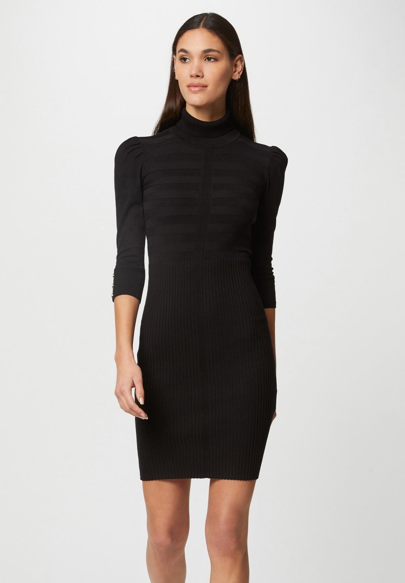 Robe tricotée noire à côtes avec un col haut, une silhouette ajustée, des manches bouffantes et un motif à rayures verticales sur le buste.