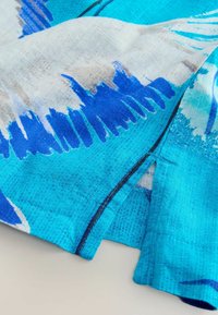 Multifarvet stof med blå og turkis abstrakte mønstre og en struktureret overflade. Kanterne er pænt syet og foldet.