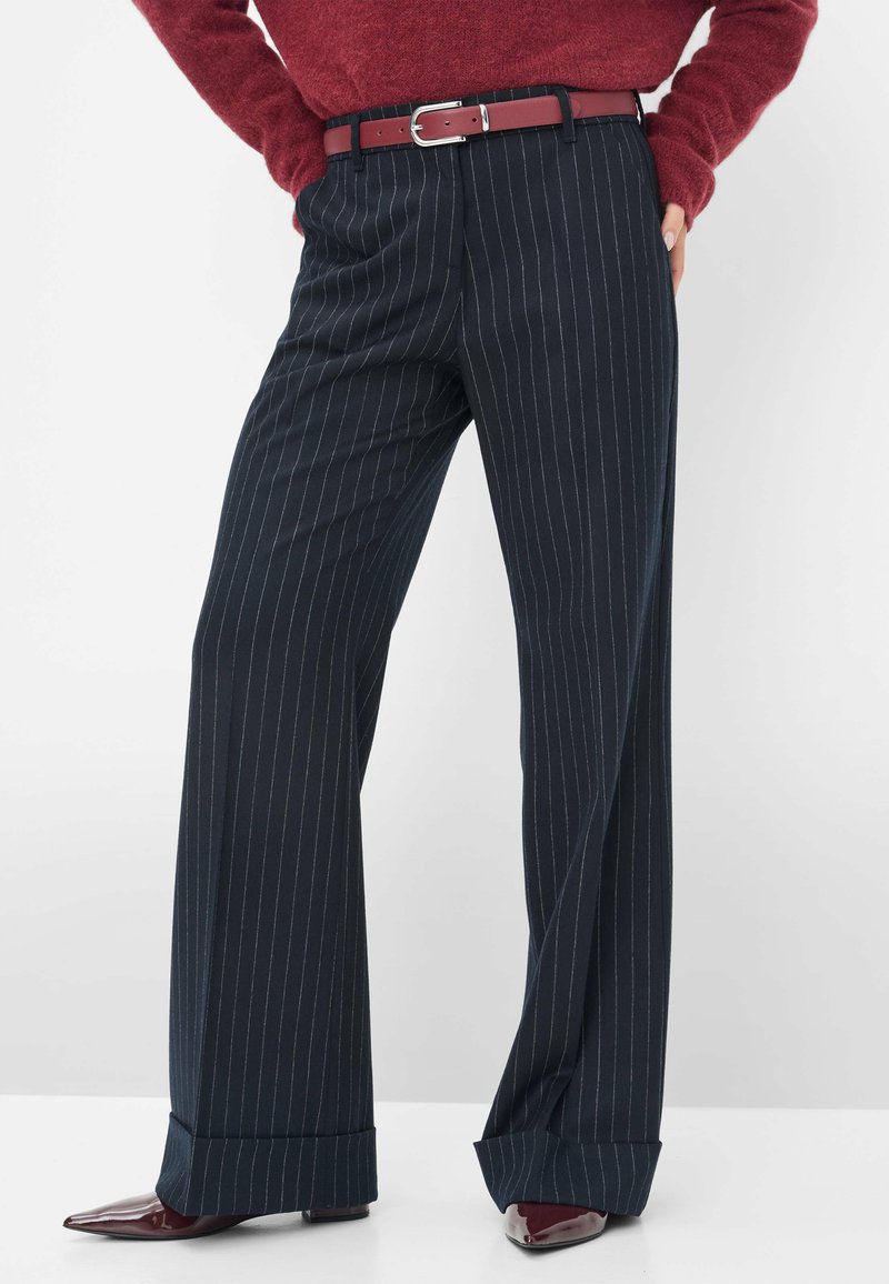 Brede, gestreepte broek in donkerblauw, vervaardigd uit een soepele stof. Voorzien van een zilveren riemgesp en een bordeauxleren riem.