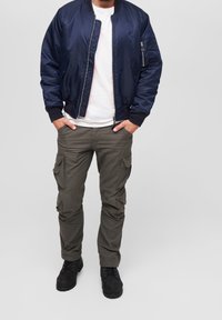 Námořnická bombarďácká bunda s hladkým materiálem, žebrovanými manžetami a bočními kapsami, zkombinovaná s olivovými cargo kalhotami s několika kapsami a volným střihem.