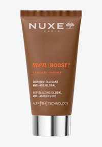 Brun plasttub med en silvermetallisk bas, märkt "NUXE Paris men [BOOST]³," med vit och orange text samt en texturerad topp.