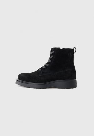Black suede ankle boots with a textured surface, round toe, gray laces, and a sturdy black sole. Features a small pull tab at the back.