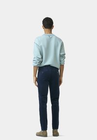 Lichtblauwe sweatshirt met opgerolde mouwen, gecombineerd met marineblauwe corduroypantalons. Model gezien van achteren, met beige schoenen.