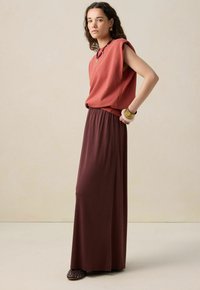 Un haut sans manches couleur rouille associé à une longue jupe bordeaux foncé. La tenue présente des tissus doux et une silhouette décontractée.