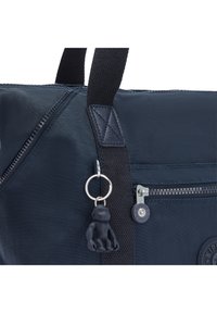 Marineblauwe stoffen tas met een ritsvak, een gestructureerde zwarte schouderband en een sleutelhanger met een klein zwart aapje.