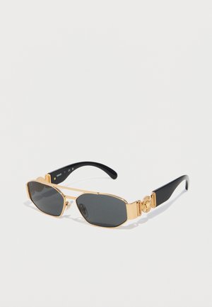 Lunettes de soleil rectangulaires noires avec montures en métal doré et accents décoratifs dorés sur les branches noires, présentées sur une surface blanche.