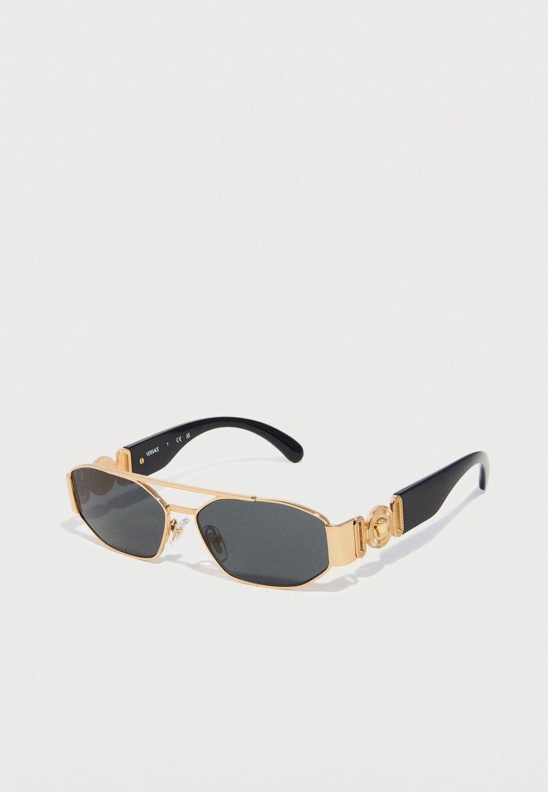 Ορθογώνια μαύρα γυαλιά ηλίου με χρυσό μεταλλικό πλαίσιο και διακοσμητικές χρυσές λεπτομέρειες στους μαύρους βραχίονες, τοποθετημένα πάνω σε λευκή επιφάνεια.