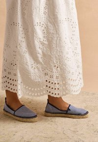 Blaue und weiße gestreifte Espadrilles mit einer geflochtenen Jutesohle und flachem Absatz, kombiniert mit einem langen weißen bestickten Kleid.