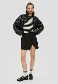 Zwarte gewatteerde jas, gestreepte zwart-witte trui, zwarte wikkelrok en zwarte loafers met dikke zolen en gestreepte sokken.