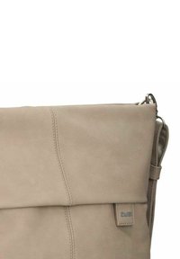 Borsa a tracolla in pelle beige con texture liscia, design a ribalta, cuciture sottili e una tracolla laterale. Presenta un piccolo tag con logo.