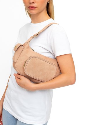 Beige Wildleder Schultertasche mit verstellbarem Trageriemen, ausgestattet mit einer Frontklapptasche und einer seitlichen Ziptasche. Glatte Textur und minimalistisches Design.