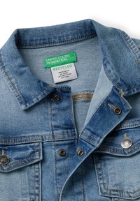 Jeansjacke in Hellblau, mit klassischem Kragen, Metalldruckknöpfen und einem Etikett, das auf recycelte Materialien hinweist, innen.