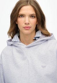 Sudadera con capucha de color gris claro, con un corte relajado, tejido texturizado y un pequeño logo de "Superdry" en hilo a juego en la parte delantera.