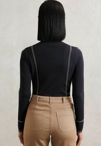 Czarny longsleeve z kontrastującymi, jasnymi szwami wzdłuż szwów, w połączeniu z beżowymi spodniami o wysokim stanie z tylnymi kieszeniami.