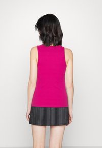 Aansluitend mouwloos topje in felroze, met een effen structuur. Gecombineerd met een zwarte pinstripe rok, zichtbare zoomlijn ter hoogte van het midden van de dij.