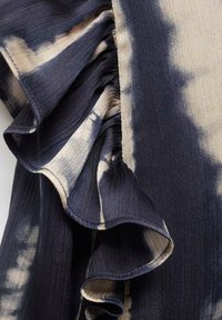 Tessuto blu scuro con motivo tie-dye crema, caratterizzato da bordi arricciati e una finitura testurizzata. Dettaglio ravvicinato del design e della texture.