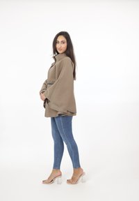 Beige, överdimensionerad cape-jacka med hög krage, tillsammans med åtsittande blå jeans. Klara blockklackar framhäver looken.