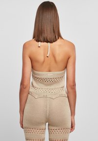 Top bandeau de punto en beige con detalles de ganchillo, que presenta una cinta de atar en la parte posterior y un cuerpo texturizado. Silueta ajustada con un sutil borde en forma de ondas.