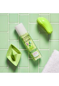 Groene Revlon Kids conditioner sprayfles met witte dop, gestructureerd, naast een groene ontklitborstel en een driehoekig groen doosje op mintgroene tegels.