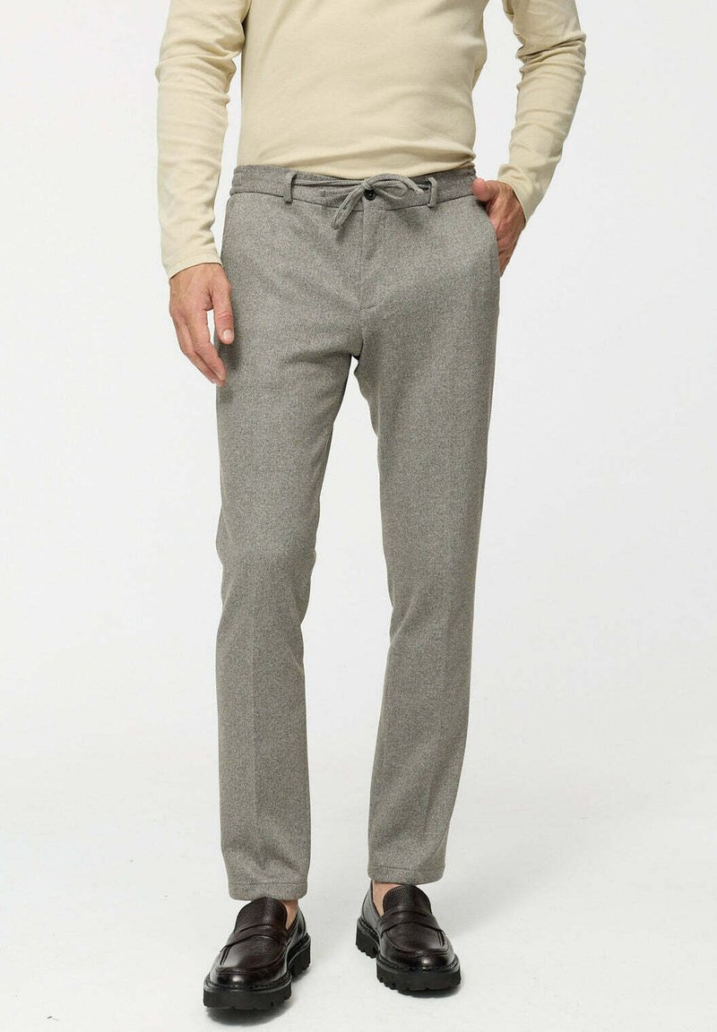 Grijze geweven broek met een slim fit, elastische trekkoord taille en voorkruipzakken. Gecombineerd met donkerbruine instappers.