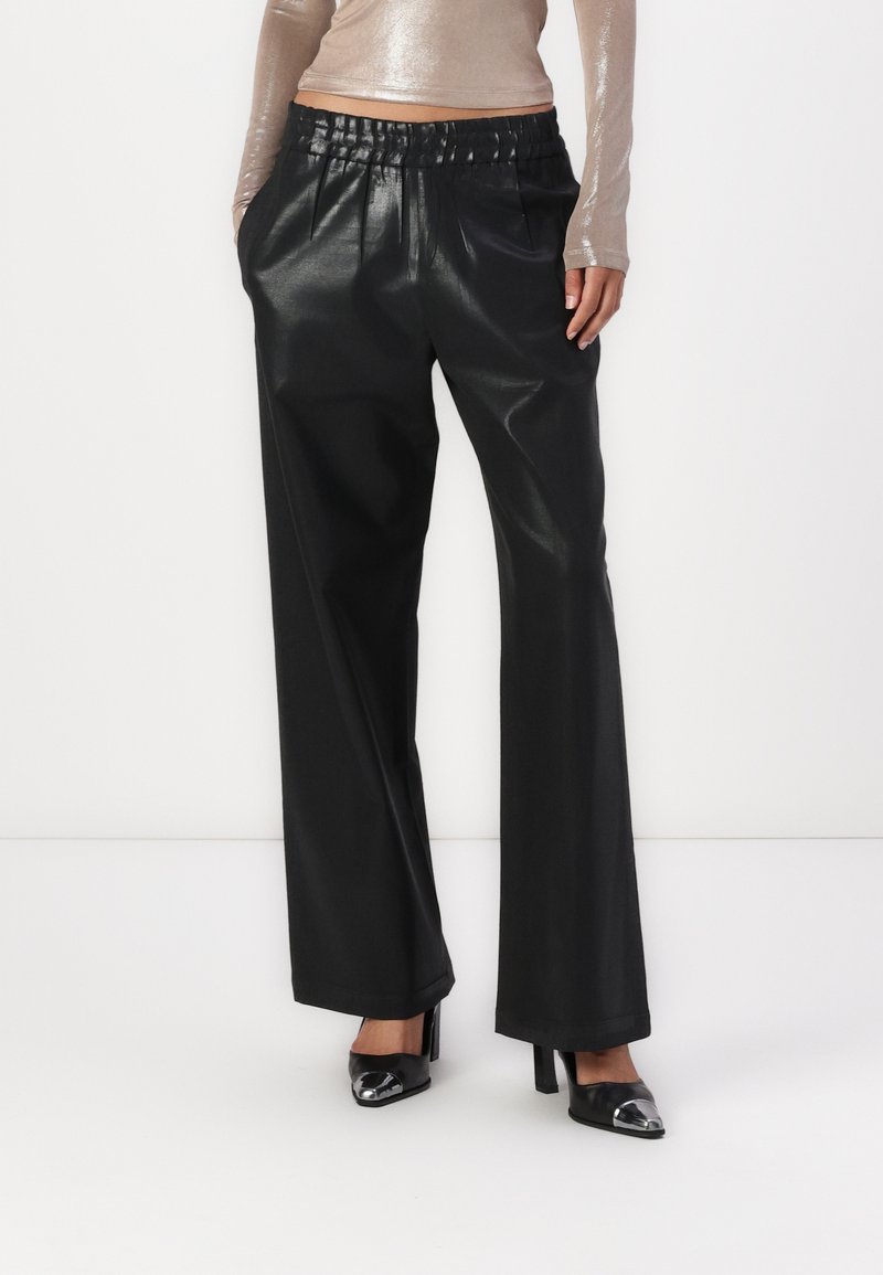 Zwarte faux leren wijde broek met een geplooide tailleband. Gepaard met zwarte hakken. Gladde, glanzende textuur.