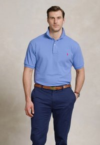 Svijetloplavi polo majica s kragnom, kratkim rukavima i malim crvenim logom konjića. Uparen s tamnim hlačama i smešnim kožnim pojasom.