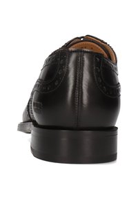 Scarpa elegante nera in pelle con dettagli brogue, tacco visibile e cucitura lungo il retro, mostrata da un angolo posteriore su sfondo bianco.