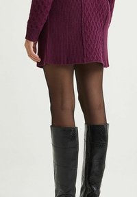 Robe tricotée violette avec un motif en losanges texturé, accompagnée de bottes noires jusqu'aux genoux, brillantes avec une texture peau de serpent, et des collants noirs transparents.