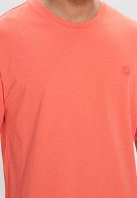 T-shirt in cotone corallo con maniche corte, colletto a girocollo, caratterizzato da una sottile grafica del sole in un colore abbinato sul petto.
