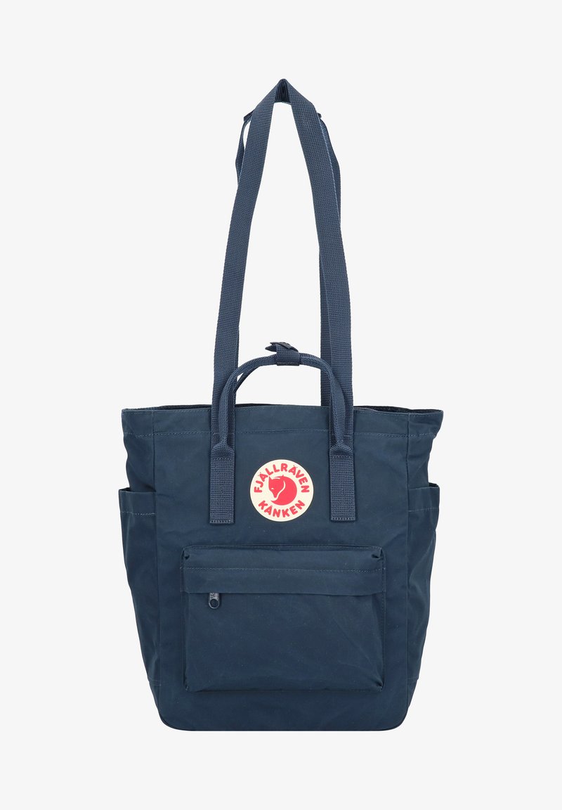 Borsa tote blu navy con due manici lunghi, una tasca frontale con zip e una toppa rotonda con logo. Realizzata in tessuto resistente con finitura testurizzata.